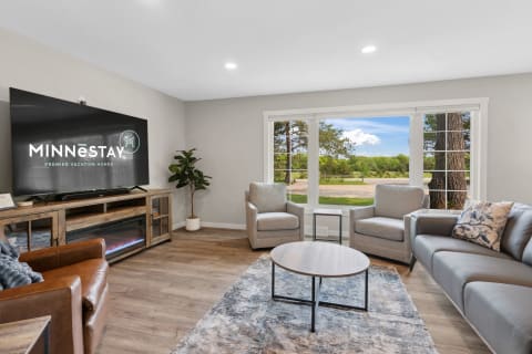 A contemporary living room with a grey sofa, two armchairs, a round coffee table, and a large TV.