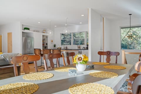 A dining table with yellow placemats and a vase of sunflowers in a bright open kitchen space.