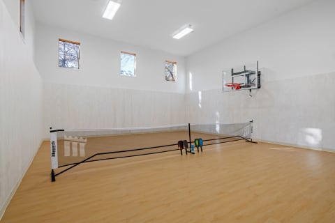 An indoor sports room with a basketball hoop and a badminton net set up.