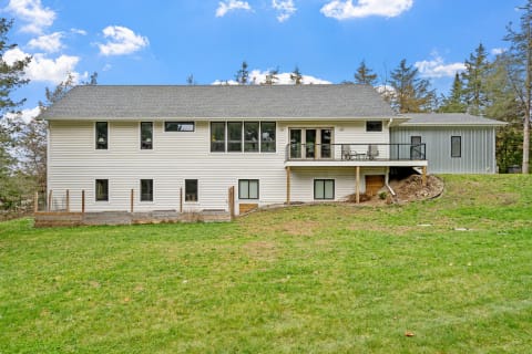A two-story house with white siding and a balcony, set in a natural landscape.