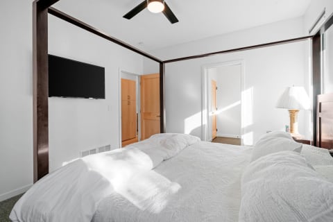 Modern bedroom with a white bed, bedside lamp, and wall-mounted television.