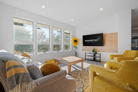 A modern living room with a gray sofa, yellow accent chairs, and large windows.