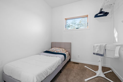 Minimalist bedroom featuring a single bed, colorful bedding, and a white stand with a towel.