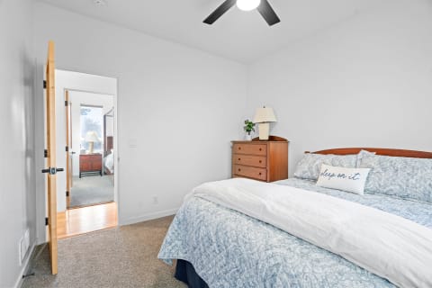 Cozy bedroom with blue quilted bedding, a wooden dresser, and an open door leading to another room.