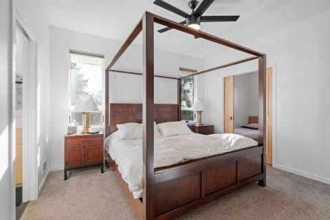 A cozy bedroom featuring a four-poster bed, wooden nightstands, and large windows with natural light.