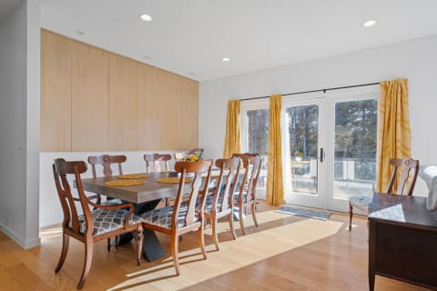 A bright dining room featuring a wooden table, chairs with patterned cushions, and yellow curtains.