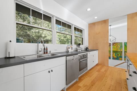 Contemporary kitchen with white cabinets, stainless steel appliances, and a view of nature outside.