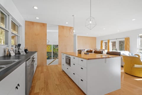 A bright kitchen featuring white cabinetry, a wooden countertop, and geometric pendant lights.