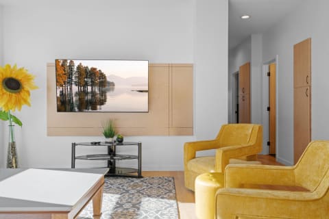 Stylish living room featuring yellow chairs, a mounted TV displaying a tranquil landscape, and a sunflower.