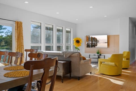 Open living and dining area featuring a sofa, yellow chairs, and large windows.