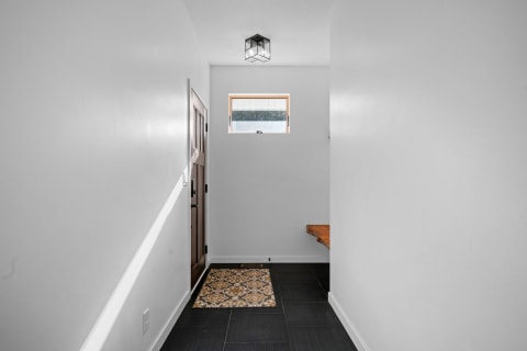 Interior hallway featuring white walls, a wooden door, natural light, and a patterned rug.