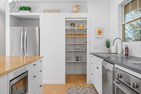 Modern kitchen featuring stainless steel appliances and a decorative pantry with glassware.