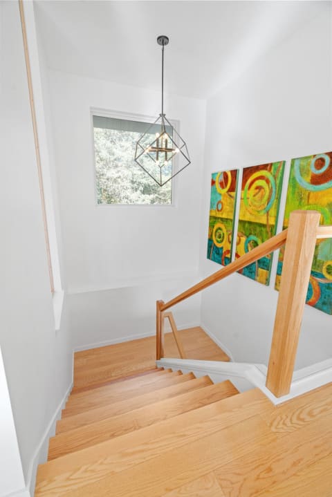 Staircase with wooden steps, modern pendant light, and colorful abstract art.