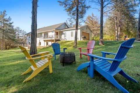 Colorful Adirondack chairs and a fire pit on a green lawn in front of a modern house.