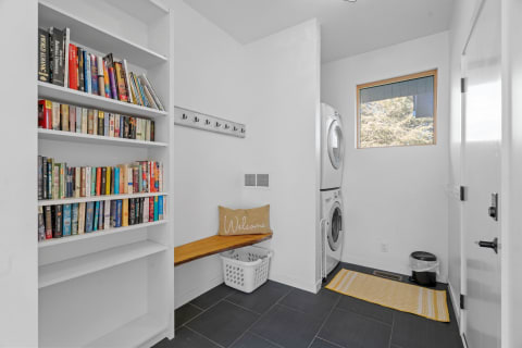 A clean laundry room with bookshelves, a bench, and washing machines.