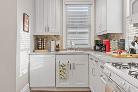 A bright and modern kitchen featuring white cabinets, a granite countertop, and coffee equipment.