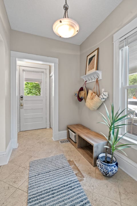 An entryway with a wooden bench, decorative plant, and bags hanging on the wall.