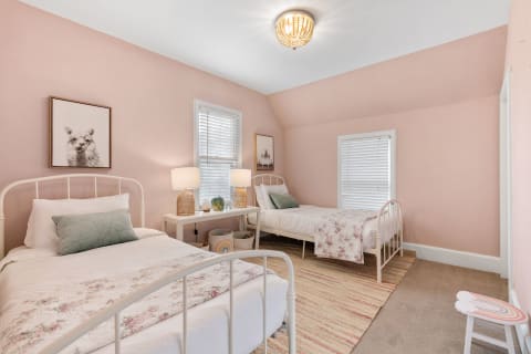 A beautifully designed bedroom with two beds in white metal frames, soft pink walls, and llama artwork.