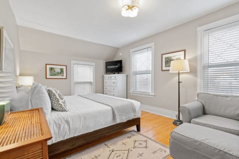 A well-decorated bedroom featuring a bed, dresser, television, and seating area.