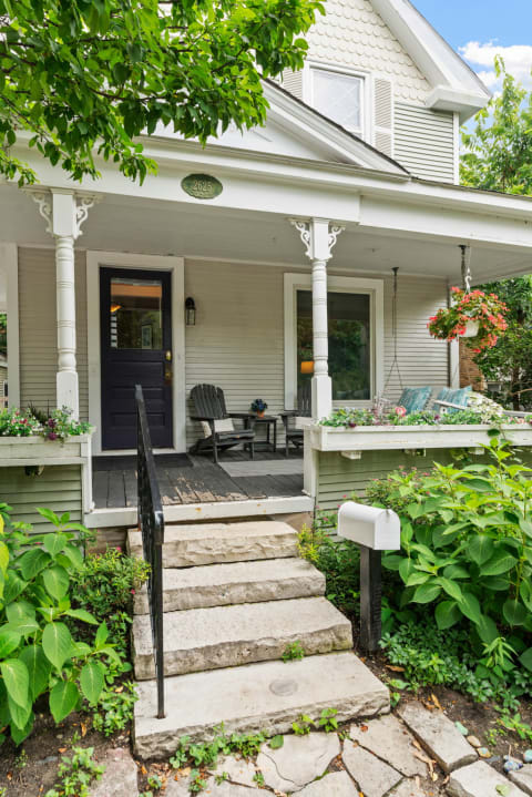 A traditional house front porch with stone steps, plants, and outdoor seating.
