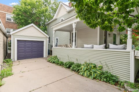 A house with a porch, purple garage, and surrounding greenery.