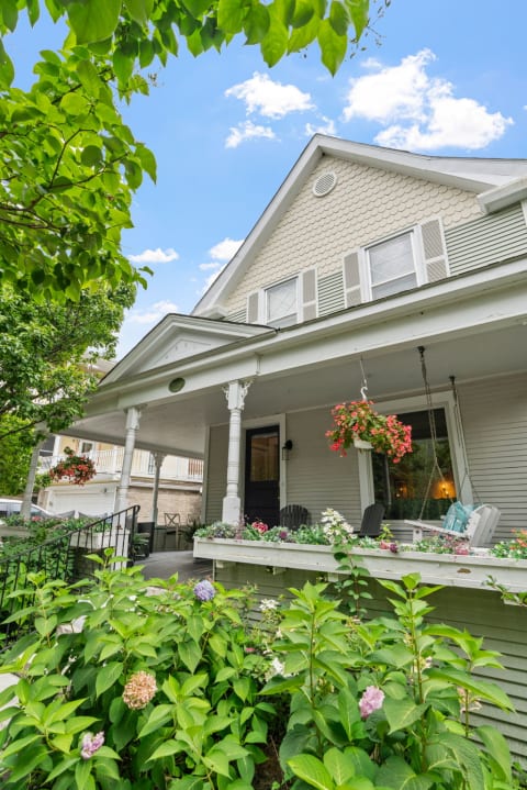 Charming two-story house with a welcoming porch and vibrant flower beds.
