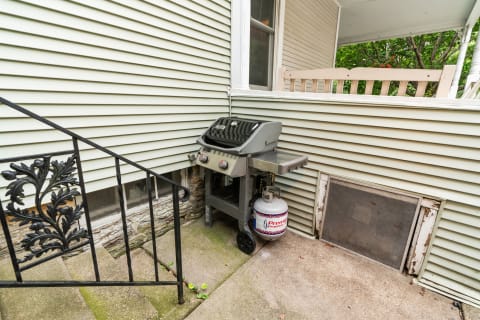 Gas grill with propane tank beside a house with vinyl siding and stone steps.
