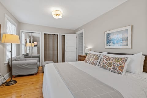 Cozy bedroom with white linens, decorative pillows, and a gray armchair.