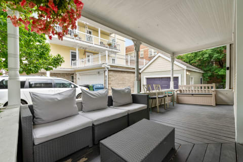 Cozy porch arrangement with gray couches, a coffee table, and a view of a yellow building.