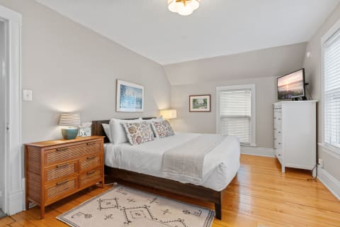 Cozy bedroom with a queen-sized bed, wooden dresser, and natural light through the window.