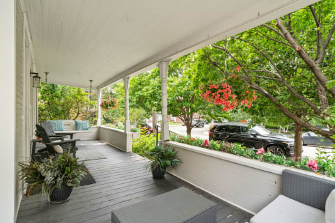 Charming front porch featuring rocking chair, bench with striped cushions, and vibrant flowers.