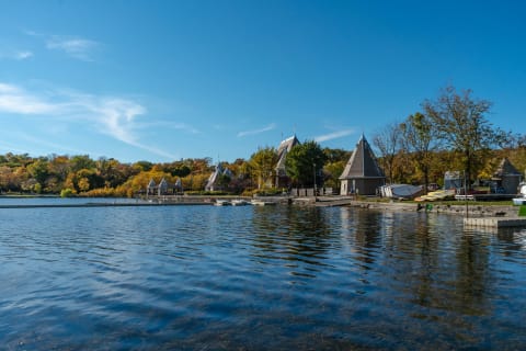 View of a lake with peaked-roof houses and fall-colored trees under a clear blue sky.