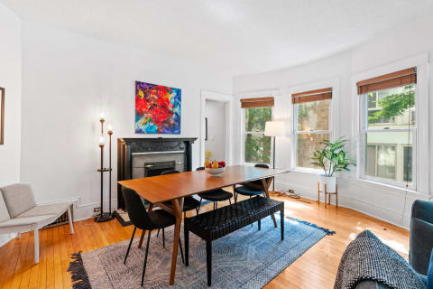 A bright dining room with a wooden table surrounded by black chairs, artwork on the wall, and lots of natural light.