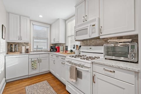 A modern kitchen featuring white cabinetry, granite countertops, and various appliances.