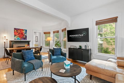 A cozy and modern living room with blue-green chairs, a brown leather sofa, and a dining area.