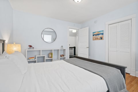 Cozy bedroom featuring a round mirror, a neatly made bed, and a beach-themed painting.