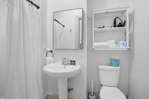 A clean and modern bathroom featuring a shower with a textured curtain, a pedestal sink with soap dispensers, and neatly arranged towels.