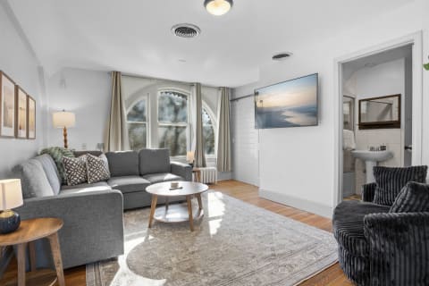 A modern den with gray seating, wooden accents, and bright natural light coming through arched windows.