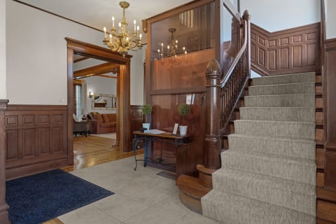 Elegant wooden entrance with a chandelier and carpeted staircase.