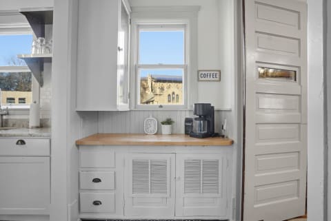 A cozy kitchen corner with a coffee maker, wooden countertop, and a view through the window.