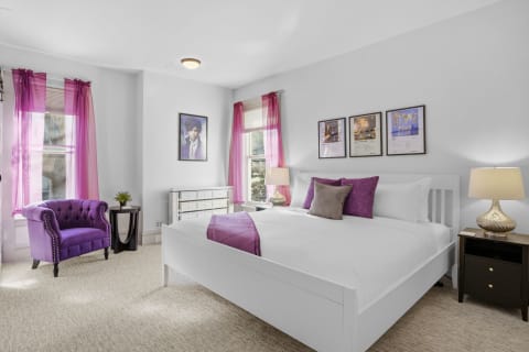 Modern bedroom with purple decor and elegant furnishings, including an armchair and framed art.