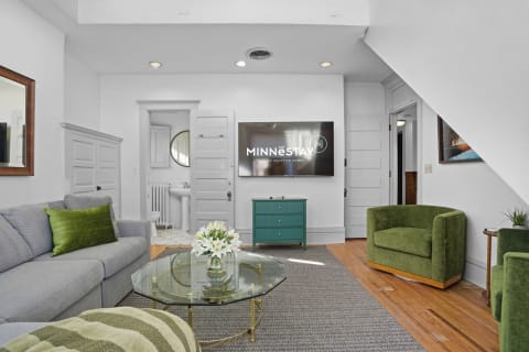 Modern living space with gray sofa, green chairs, glass coffee table, and turquoise cabinet.
