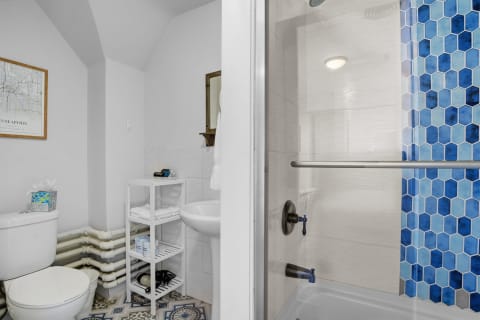 Modern bathroom with blue hexagon tiles, white toilet, and minimalist shelving.