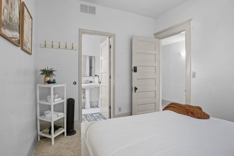 Comfortable bedroom with white linens and shelving, featuring a visible bathroom.