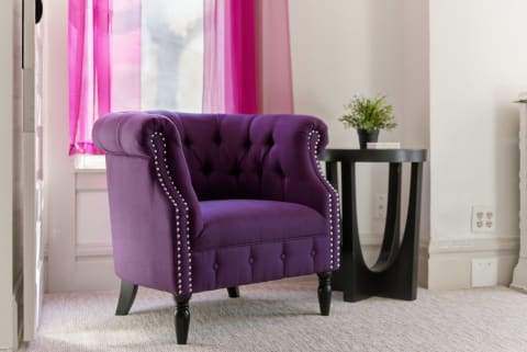A plush purple armchair next to a modern black side table, with pink sheer curtains in the background.