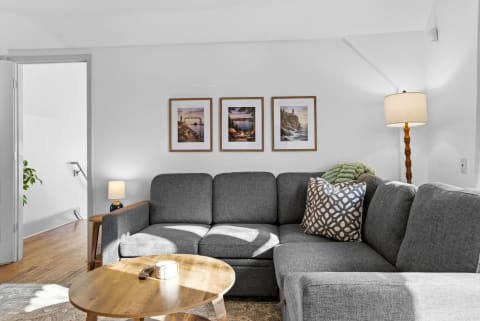 A gray sectional sofa in a bright living room with framed pictures and a wooden coffee table.
