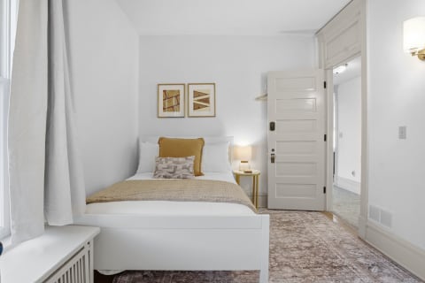 A serene bedroom with a white bed, textured beige linens, and warm lighting.