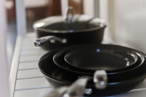 A close-up view of black cookware including frying pans and plates on a white kitchen shelf.