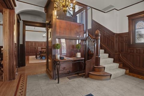 Entrance foyer featuring a wooden staircase, elegant chandelier, and rich wood paneling.