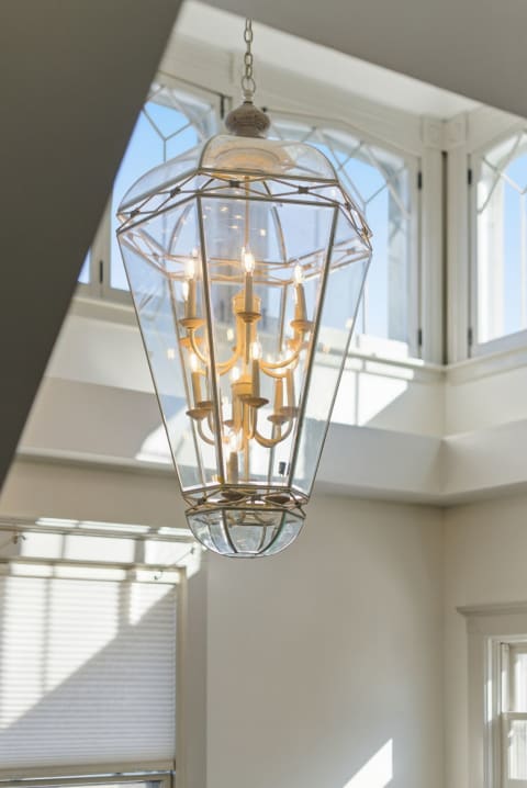 An elegant glass chandelier with candle-style bulbs hanging from the ceiling near large windows.
